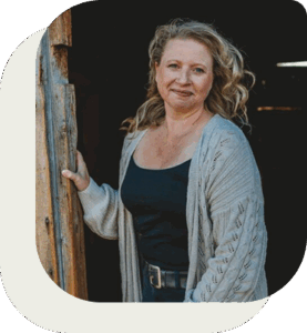 Photo of Sharon Loose at the door of a wooden shed, smiling at the camera