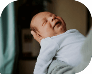 young baby smiling while asleep, in his mother's arms