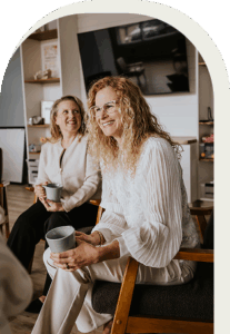 Two women sitting on chairs, holding coffee mugs and smiling